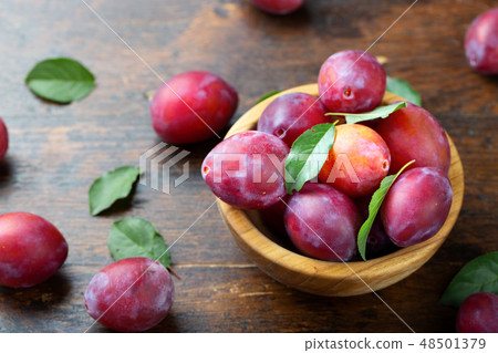 Wooden plate with ripe juicy plums on table. 48501379
