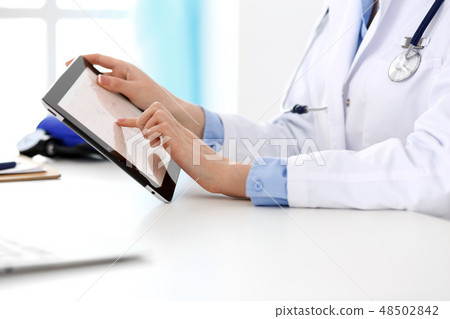 Doctor working table. Woman physician using tablet computer while sitting in hospital office close 48502842