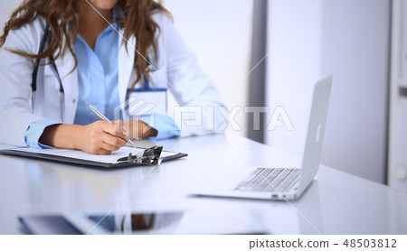 Unknown doctor woman filling up medical form while sitting at the desk in hospital office. Physician Unknown doctor woman filling up medical form while sitting at the desk in hospital office. Physician 48503812