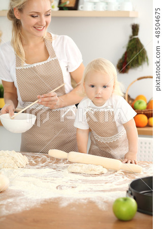 Little girl and her blonde mom in beige aprons playing and laughing while kneading the dough in Little girl and her blonde mom in beige aprons playing and laughing while kneading the dough in 48504675