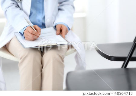 Female doctor writing up medication history records form on clipboard, while sitting at the chair Female doctor writing up medication history records form on clipboard, while sitting at the chair 48504713