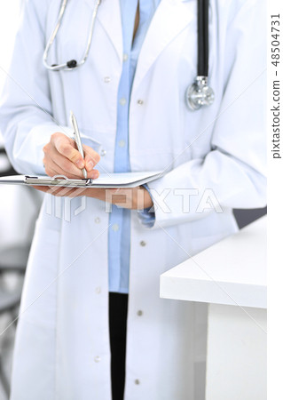 Doctor woman filling up medical form while standing near reception desk at clinic or emergency Doctor woman filling up medical form while standing near reception desk at clinic or emergency 48504731