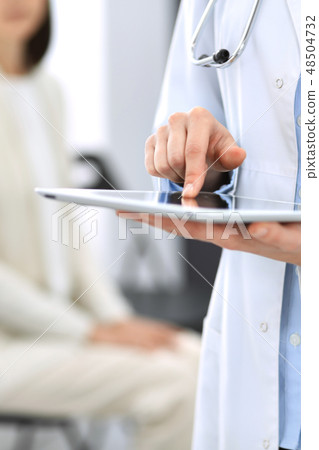 Female physician using digital tablet while standing near reception desk at clinic or emergency Female physician using digital tablet while standing near reception desk at clinic or emergency 48504732