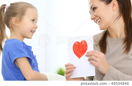 Mother's day concept. Child daughter congratulates mom and gives her postcard with red heart shape 48504848