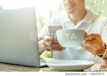Businessman looking at cell phone with hand holding coffee in coffee shop. Businessman looking at cell phone with hand holding coffee in coffee shop. 48505674
