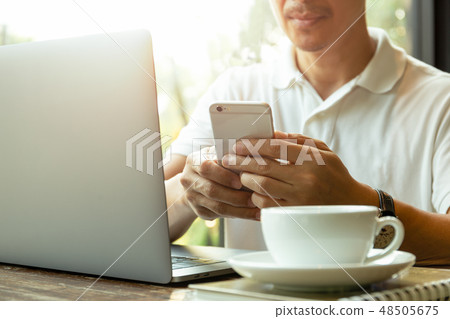 Businessman looking at cell phone with coffee and laptop on the table. Businessman looking at cell phone with coffee and laptop on the table. 48505675