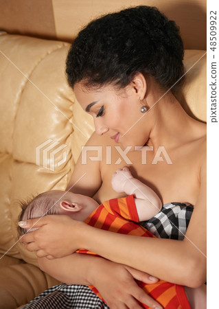 Mixed race woman breastfeeding her newborn baby on sofa 48509922