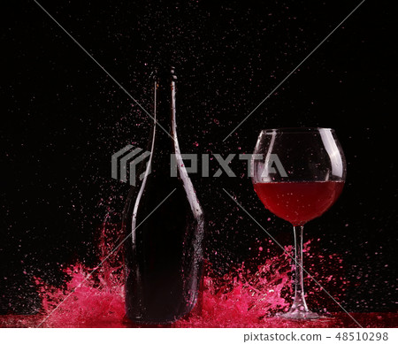 Glass and bottle of red wine splash on black 48510298