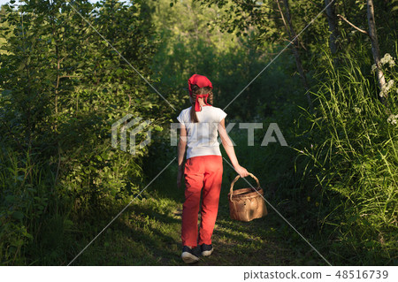 Young girl walking on a path through green woods carrying a basket 48516739