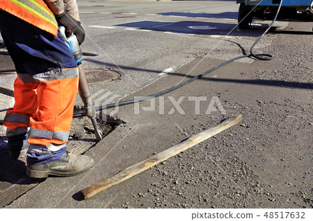 worker clears a piece of asphalt with jackhammer 48517632