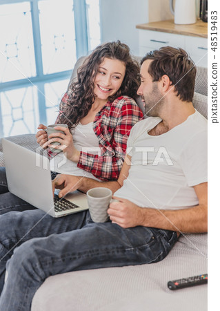 Smiling young couple enjoying morning coffee with a computer while sitting on the couch at home 48519483