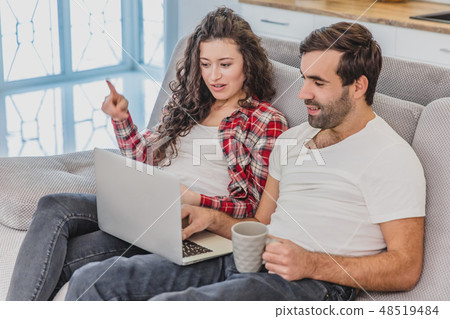 Smiling young couple enjoying morning coffee with a computer while sitting on the couch at home 48519484