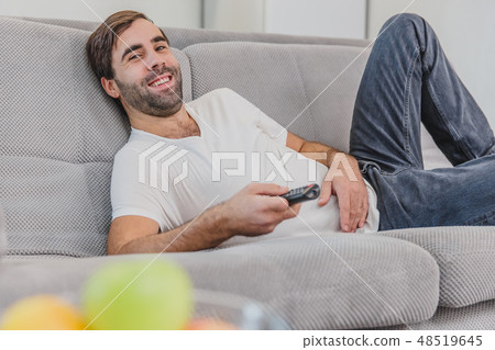Beautiful hilarious young man holding a remote control. During this time he looks at the camera 48519645