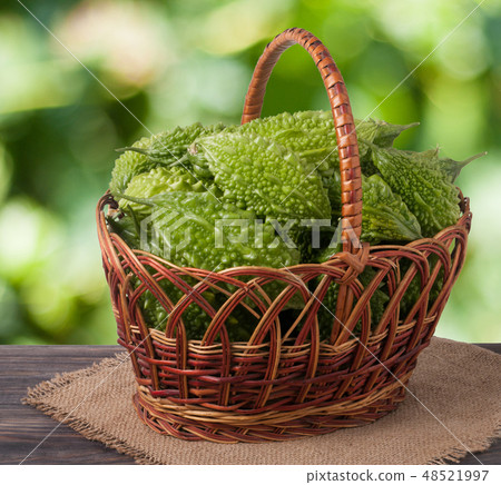 bitter melon or momordica in a wicker basket on wooden table with blurred background 48521997