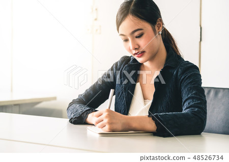 Beautiful young Asian woman writes on notebook. Beautiful young Asian woman writes on notebook. 48526734