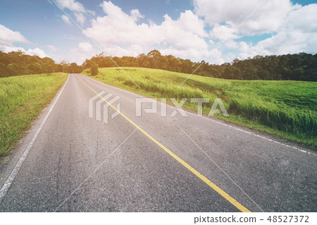 Highway road through green grass under blue sky. Highway road through green grass under blue sky. 48527372