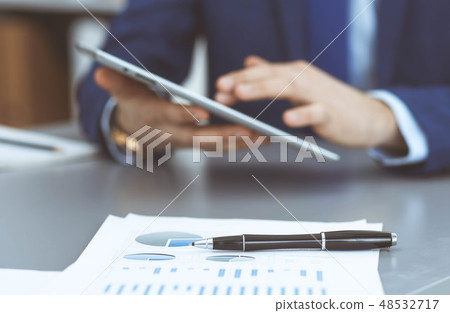 Black pen lying over business analytics papers. Businessman hands using tablet at the background Black pen lying over business analytics papers. Businessman hands using tablet at the background 48532717