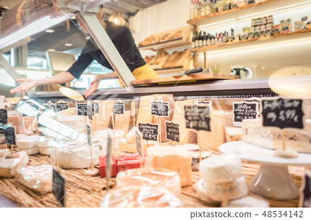 Shop clerk woman sorting cheese in the supermarket display Shop clerk woman sorting cheese in the supermarket display 48534142