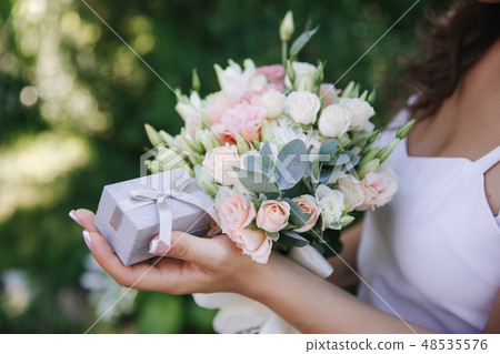 Girl hold a bouquet and ring box in hands. french manicure. Female is dressed in white dress 48535576