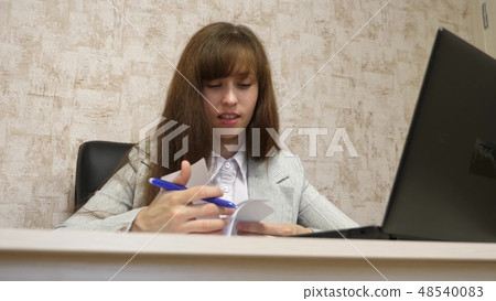 beautiful girl sitting in a chair in office and talking and making notes in bloknot. young female beautiful girl sitting in a chair in office and talking and making notes in bloknot. young female 48540083