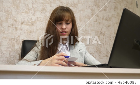 beautiful girl sitting in a chair in office and talking and making notes in bloknot. young female 48540085
