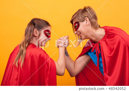 Mother and daughter dressed like superheroes playing arm wrestling over yellow background. Mother and daughter dressed like superheroes playing arm wrestling over yellow background. 48542052