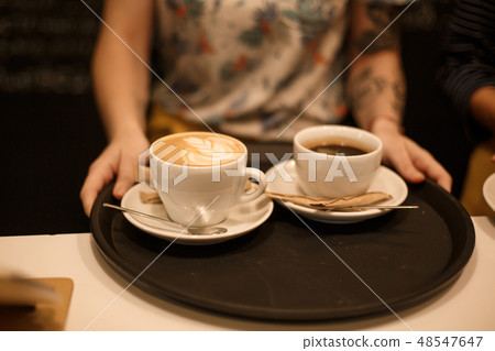 Woman bring two white cups of latte and americano Woman bring two white cups of latte and americano 48547647