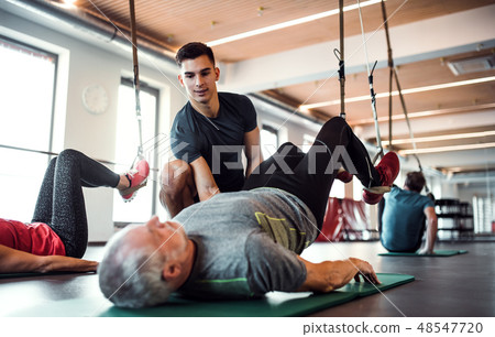 A group of cheerful seniors in gym with a young trainer doing exercise with TRX. 48547720