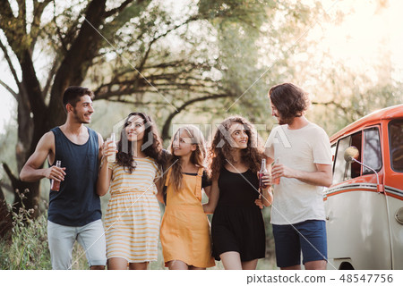 A group of young friends on a roadtrip through countryside, holding bottles and walking. A group of young friends on a roadtrip through countryside, holding bottles and walking. 48547756