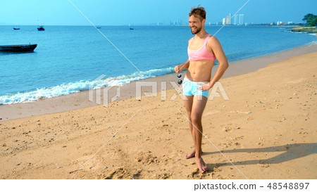 Playful handsome guy in a pink t-shirt and blue shorts rejoices at the beach. freak on the sea. Playful handsome guy in a pink t-shirt and blue shorts rejoices at the beach. freak on the sea. 48548897