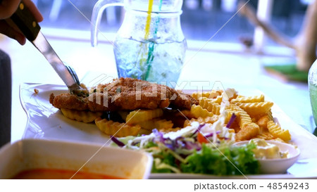 Chicken schnitzel, served with french fries and salad. someone eats french fries with a fork in a Chicken schnitzel, served with french fries and salad. someone eats french fries with a fork in a 48549243
