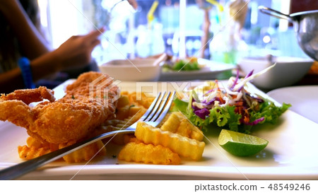 Chicken schnitzel, served with french fries and salad. someone eats french fries with a fork in a Chicken schnitzel, served with french fries and salad. someone eats french fries with a fork in a 48549246