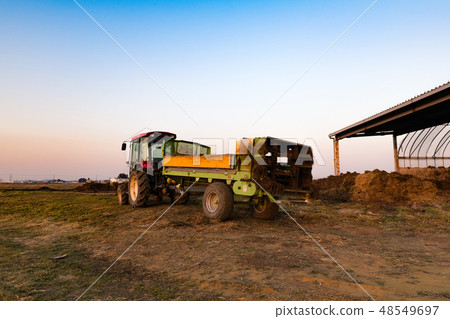 A fertilizer spreader mania spreader attached to a tractor in the setting sun 48549697