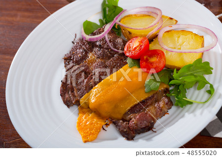 Well-done beef steak with baked potatoes and cheese served at plate Well-done beef steak with baked potatoes and cheese served at plate 48555020
