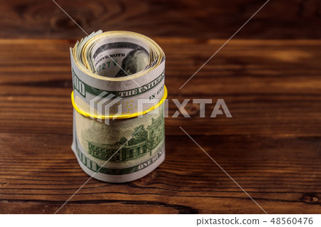 Roll of one hundred dollar bills on wooden table Roll of one hundred dollar bills on wooden table 48560476