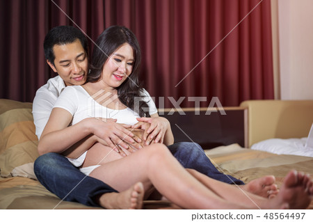 husband and his pregnant wife showing heart with hands in bed 48564497