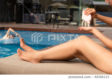 Woman applying sunscreen lotion on her hand by swimming pool on vacation. 48566125