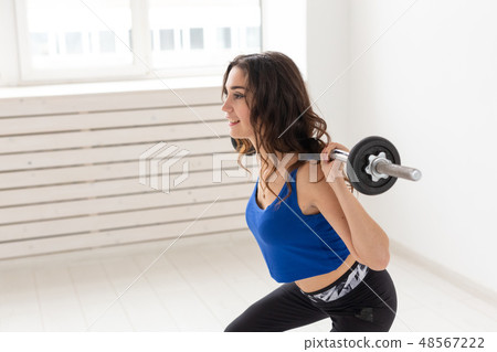 Fitness, sport and people concept - smiling sporty woman with barbell doing split squat or lunge 48567222