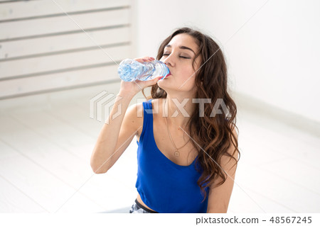 Healthy lifestyle, people and sport concept - Smiling woman sitting on yoga mat and drinking water 48567245