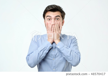 Young hispanic man covering his mouth with hand Young hispanic man covering his mouth with hand 48570417