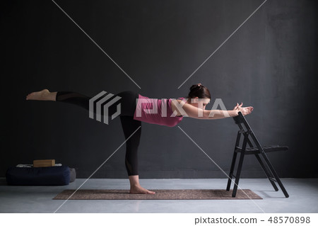 Woman show warrior asana using chair Woman show warrior asana using chair 48570898