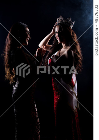 Portrait of Two Miss Asian Women Pageant Beauty Contest in Evening Ball Gown dress, look waiting final announcement moment, studio lighting dark smoke background low key exposure silhouette copy spac 48576332