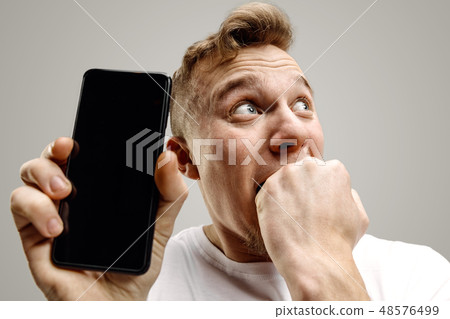 Young handsome man showing smartphone screen isolated on gray background in shock with a surprise 48576499