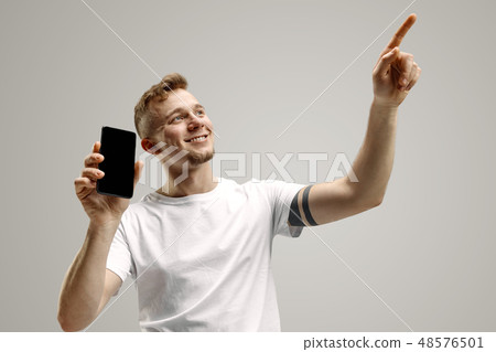 Young handsome man showing smartphone screen isolated on gray background in shock with a surprise 48576501