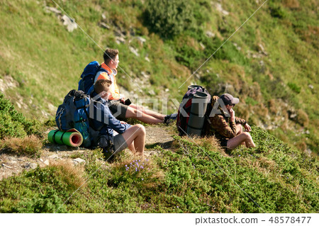 Young tourists sitting on grassy hill in mountains. 48578477