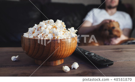 Wooden bowl with salted popcorn and TV remote. 48581870