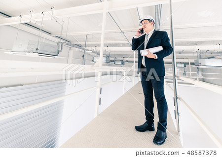 Asian engineer hold blueprint and use cellphone.. Asian engineer hold blueprint and use cellphone.. 48587378