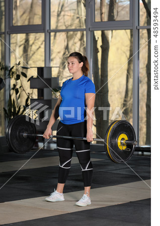 Young woman doing deadlift workout with heavy barbell in dark gym 48593494
