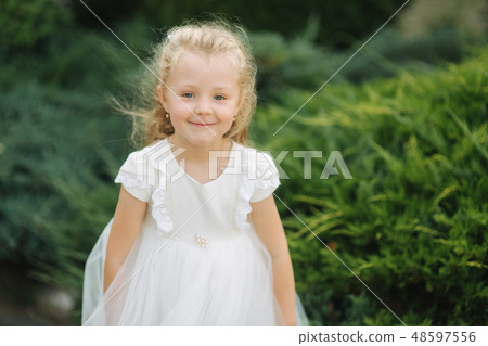 Little girl walking outside. Blond hair girl in white dress. Green background 48597556
