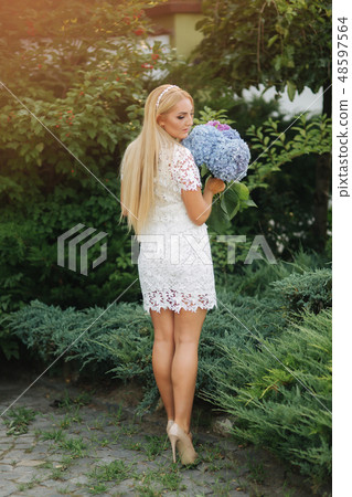Beautiful woman in white dress with bouquet of flowers. Elegant blond hair lady outside 48597564